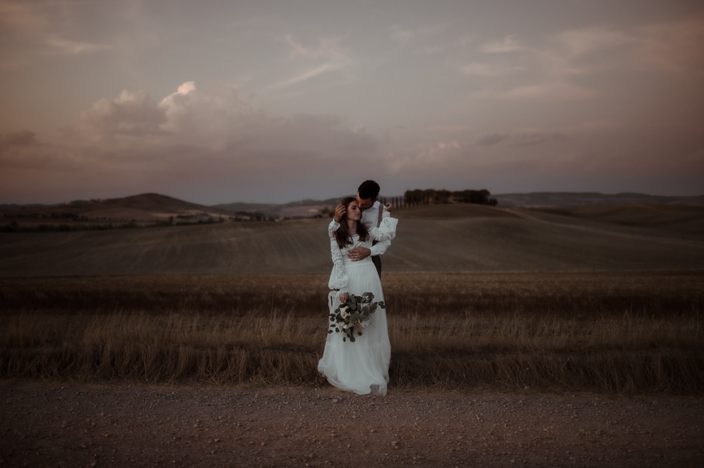 Bride and groom kissing in a field at sunset during Tuscany Elopement Guide